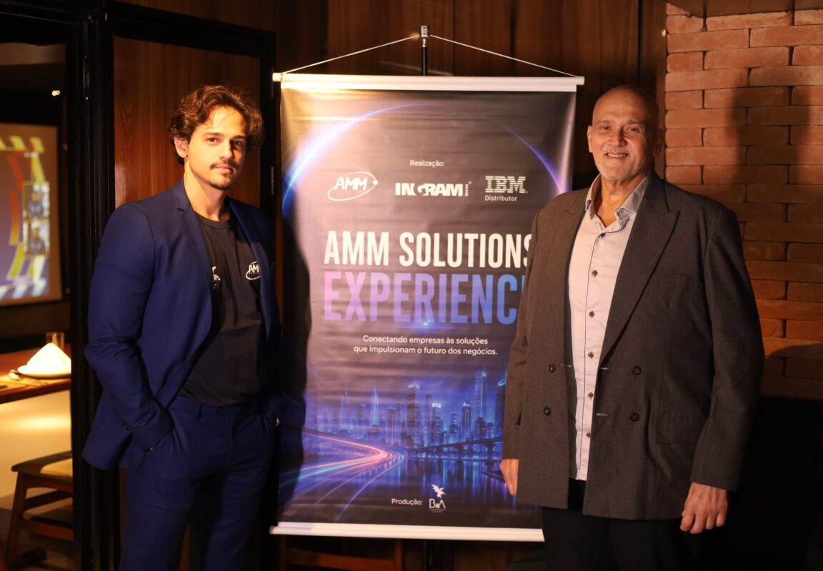 Bruno, da AMM Solutions, e um especialista convidado posam ao lado do banner do AMM Solutions Experience, evento realizado em parceria com IBM e Ingram Micro para discutir infraestrutura de TI, armazenamento de dados e Inteligência Artificial para o mercado audiovisual.